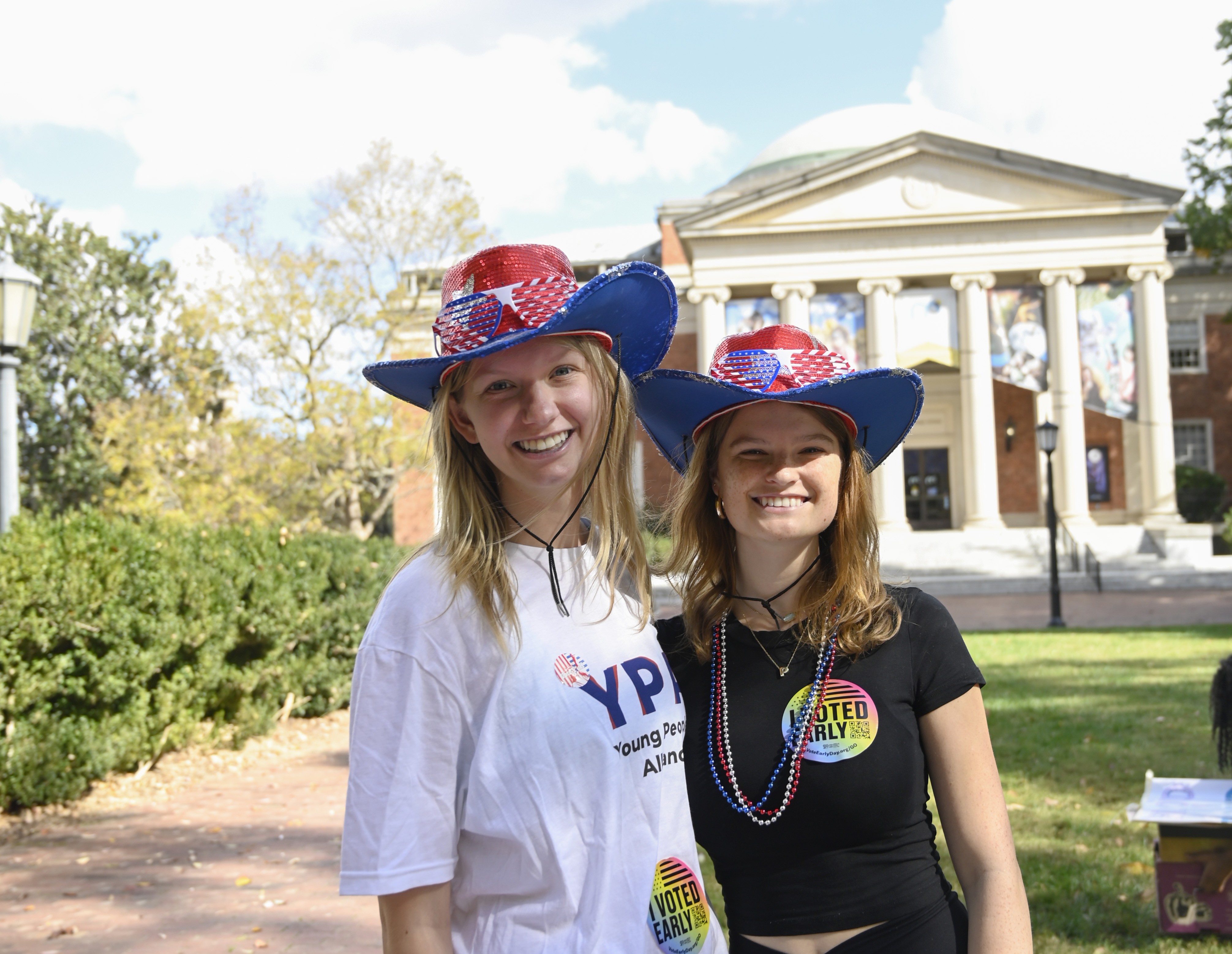 Two YPA members in patriotic hats and I Voted Early stickers on campus at UNC